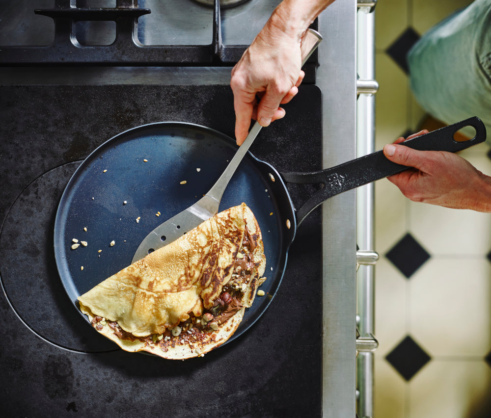 Black Steel pannenkoekenpan 26 cm met pannenkoek op kookplaat